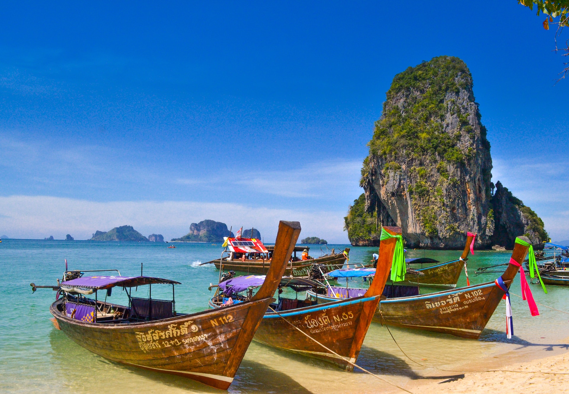 Både på Krabi-stranden, Thailand. Gruppe af farverige traditionelle longtailbåde fortøjet ved havet med skrog i lavt turkisblåt vand.