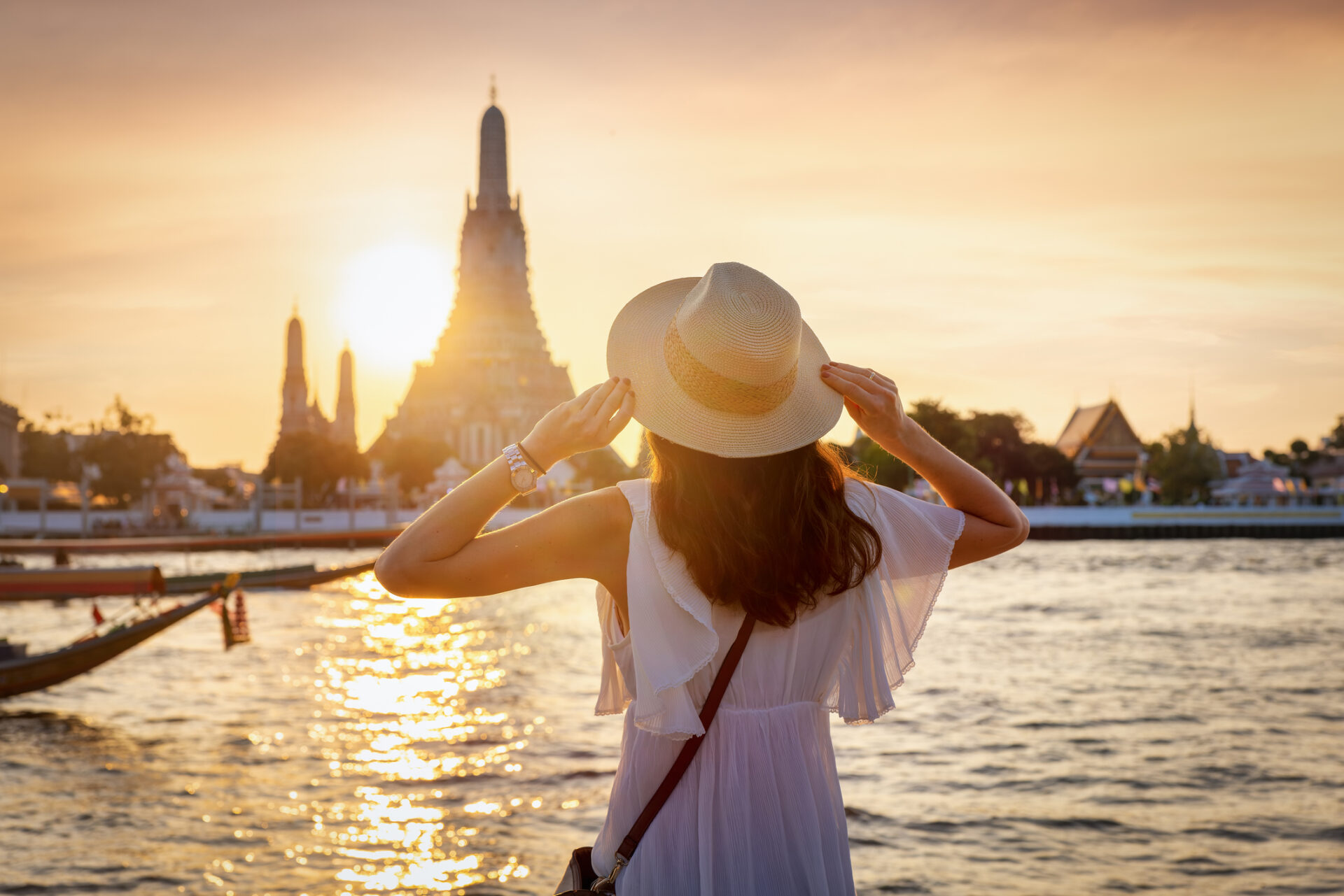 Kvinde med hat ser på solnedgang over vand i Bangkok