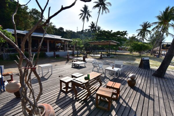 Holzterrasse mit Tischen und Stühlen am Strand des Thanya Beach Resort